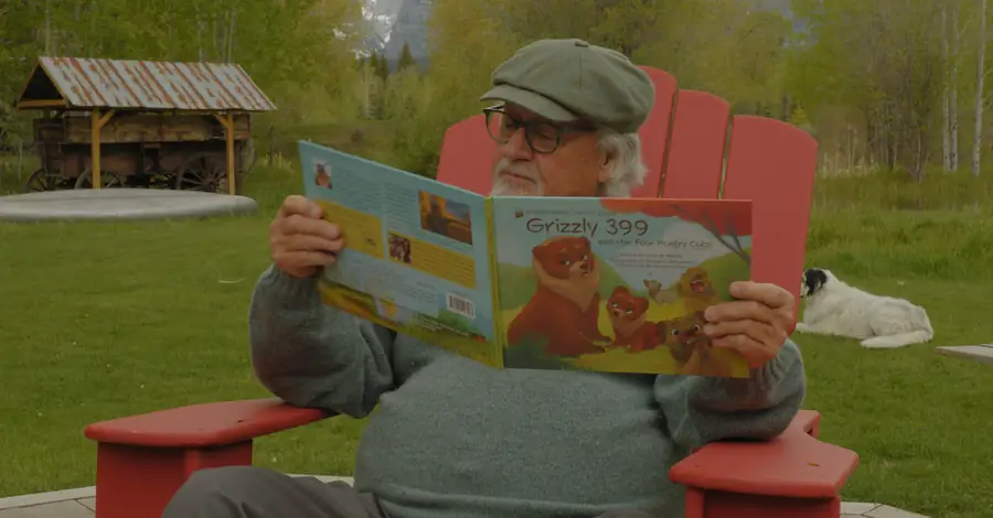 Man in a red chair reading a children's book about Grizzly 399