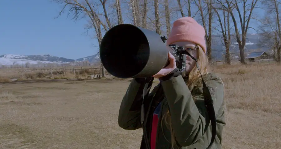 Photographer in a pink beanie looking through a long lens